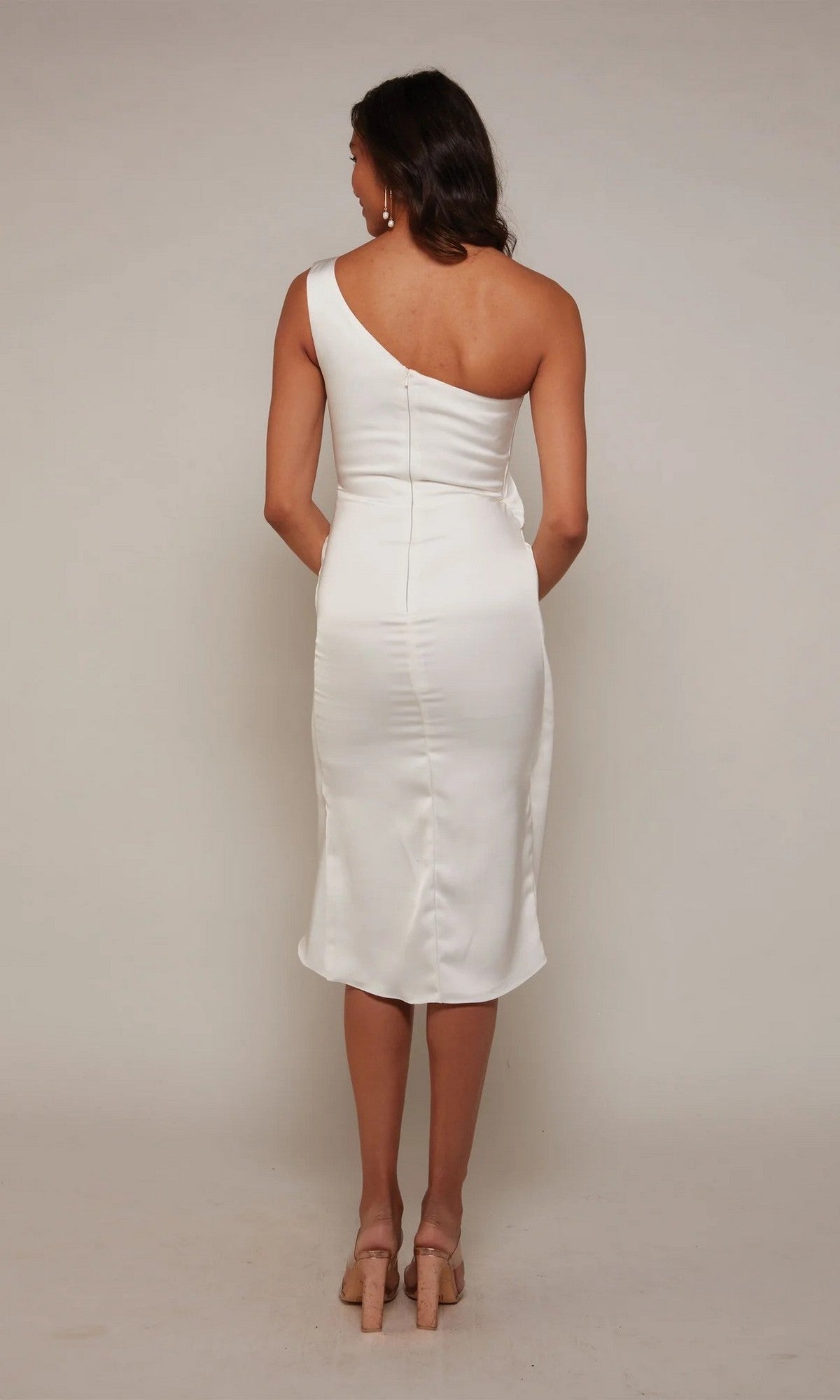 A woman faces away, wearing the Alyce 70038 knee-length white party dress and beige heels against a plain background.